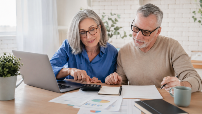 Casal de adultos analisando documentos financeiros em uma mesa com calculadora e laptop